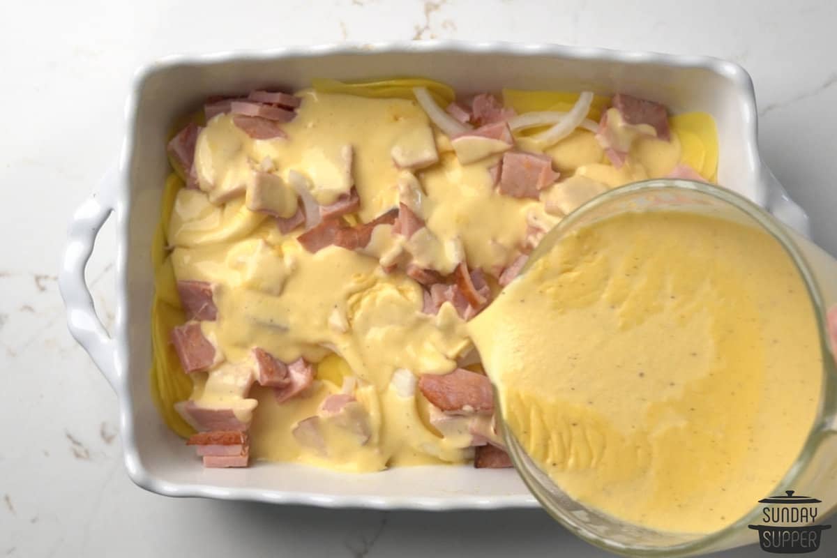 cheese sauce poured over the first layer of potatoes, onions, and ham