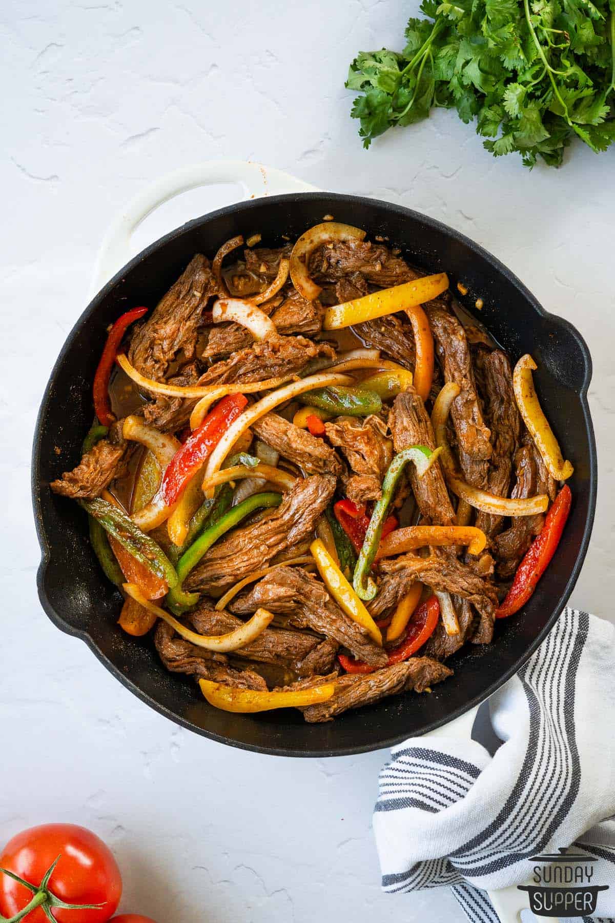 steak fajitas in a skillet with fresh herbs on the side