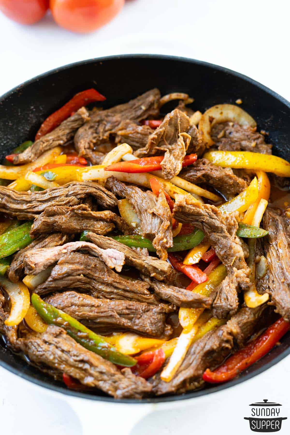 steak fajitas in a skillet with fresh tomatoes in the background