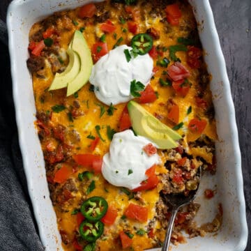 close up of taco casserole in a white casserole dish with a spoon inside