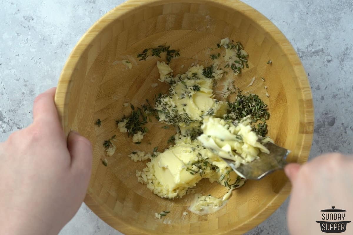 the herbs and garlic being mixed into softened butter with a fork