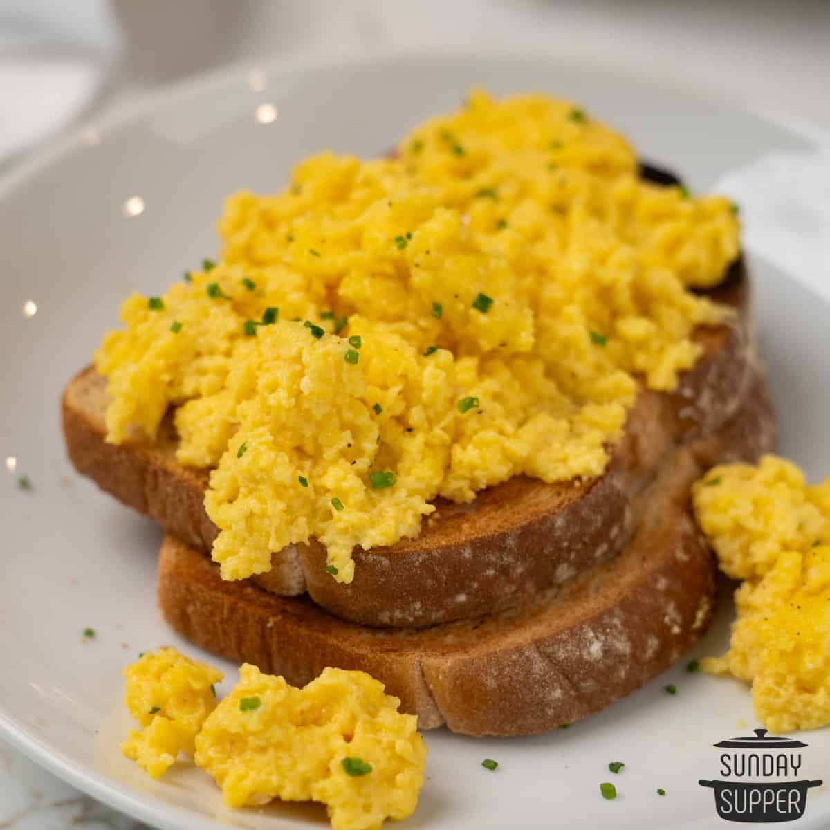 two slices of toast with a topping of creamy scrambled eggs