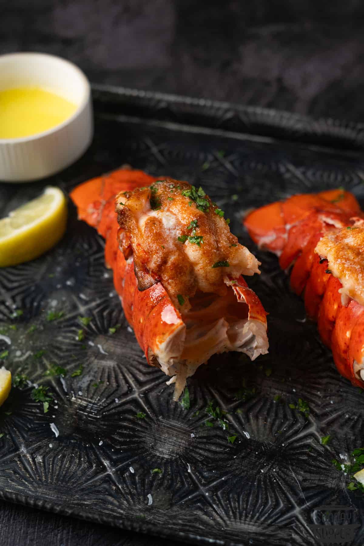 two lobster tails on a platter with lemon and butter