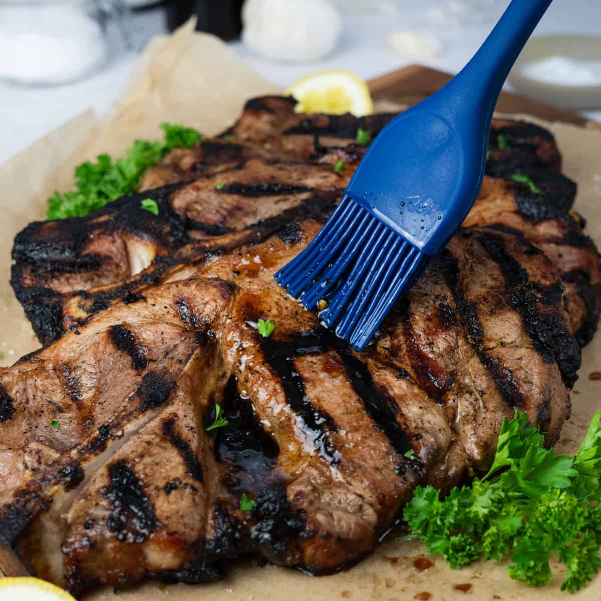 extra marinade being brushed on to grilled pork steaks