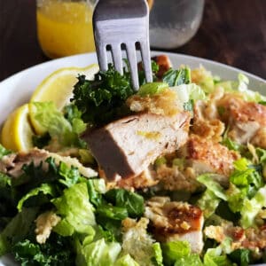 a fork taking a piece of marinated chicken from a bowl of salad