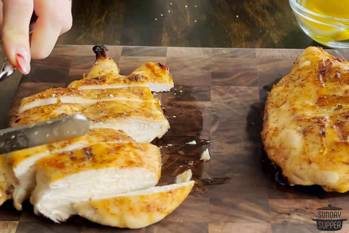 marinated chicken being sliced on a cutting board