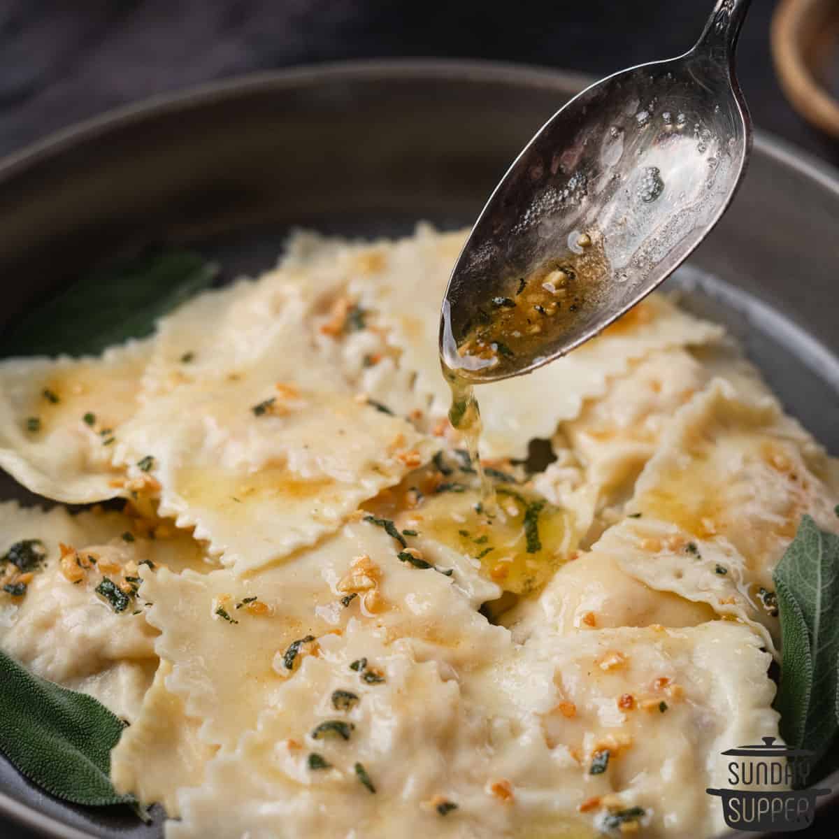 pouring sage butter sauce over lobster ravioli in a bowl