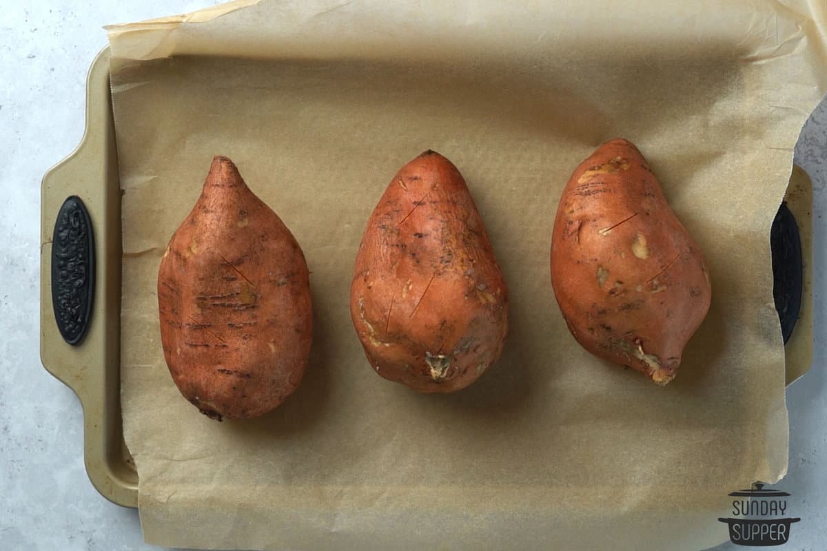 sweet potatoes scrubbed and pierced on a baking sheet