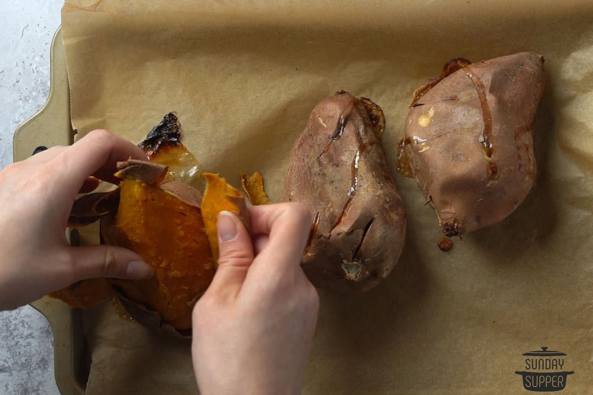 baked sweet potatoes being peeled on a baking sheet