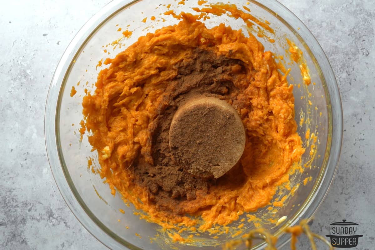 brown sugar and seasonings being added to the bowl of sweet potatoes