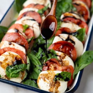 balsamic glaze being poured over a tray of tomato mozzarella salad