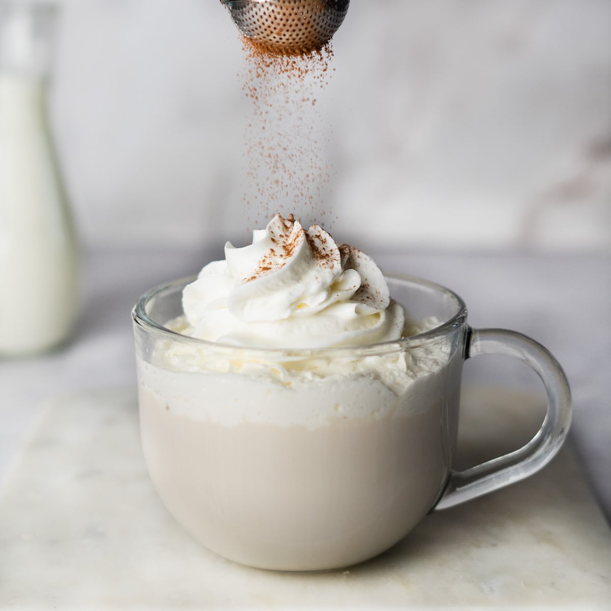 sprinkling cinnamon over top of a white chocolate mocha