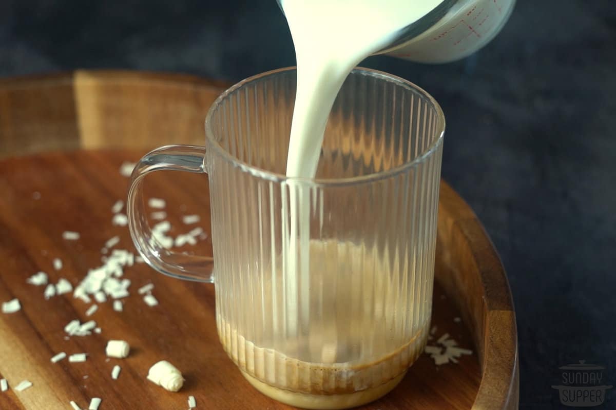 adding steamed milk to a clear mug