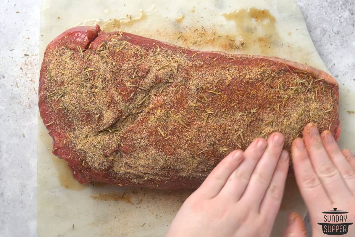 seasoning being patted down over the chuck roast