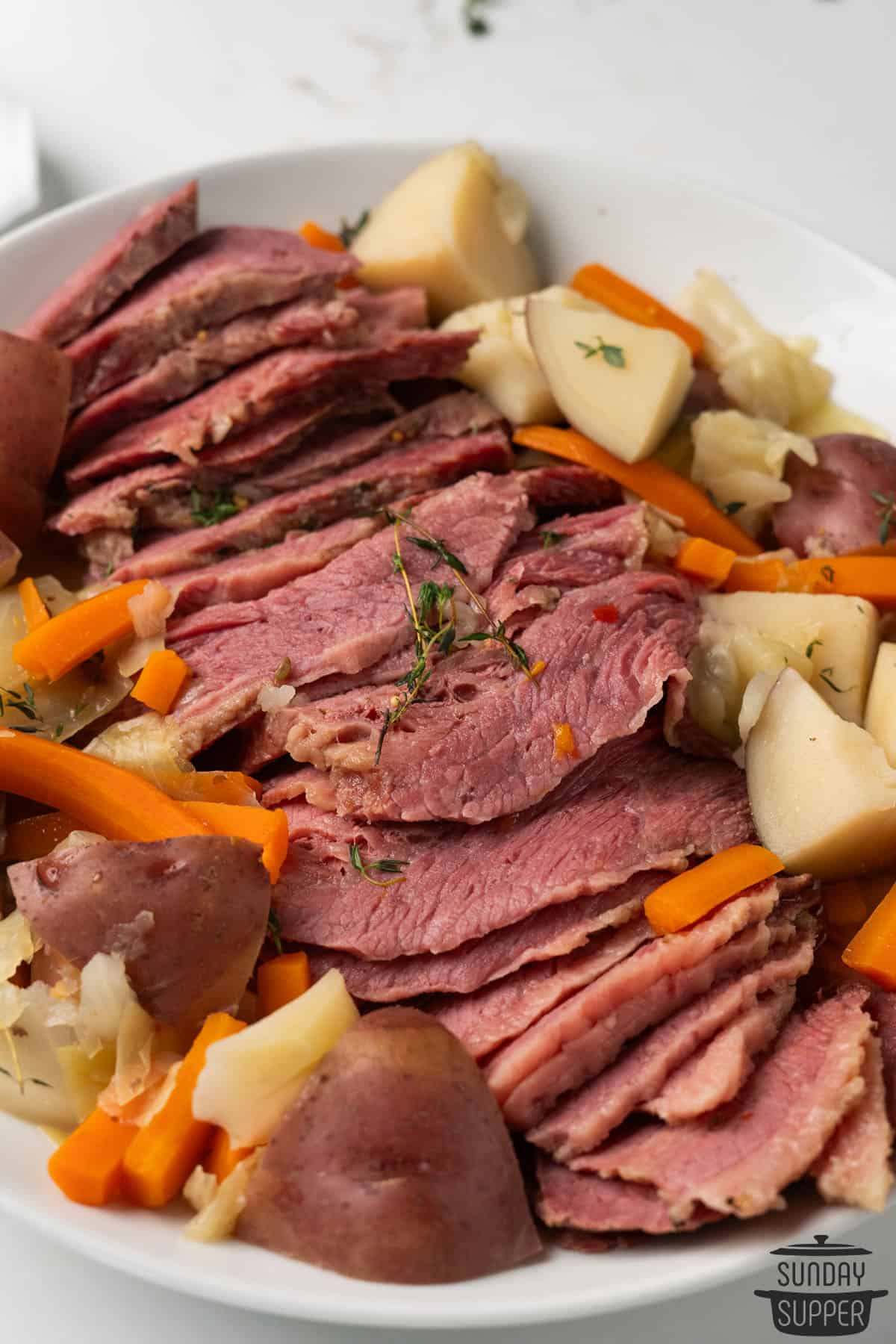sliced corned beef on a plate with extra veggies and thyme