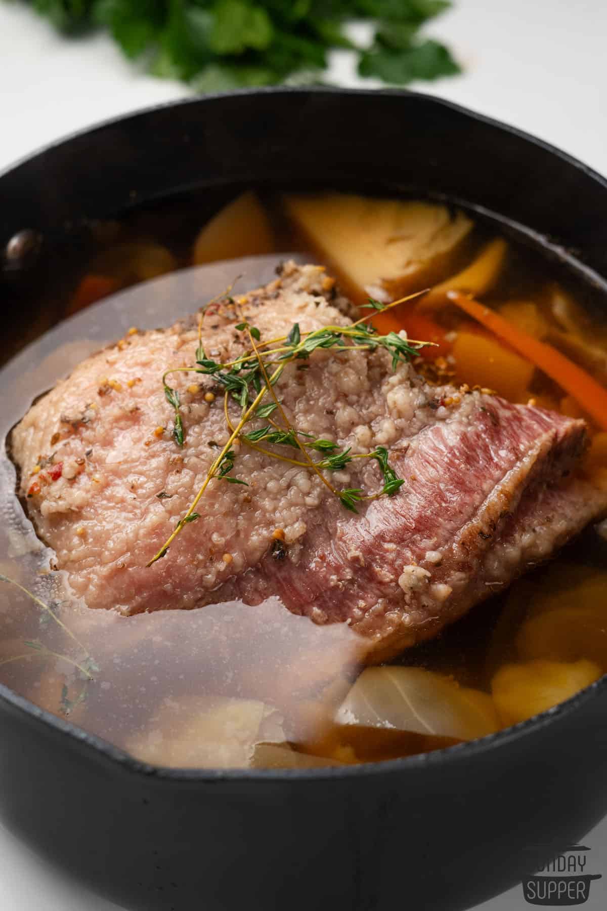 corned beef in a pot of broth and veggies with thyme