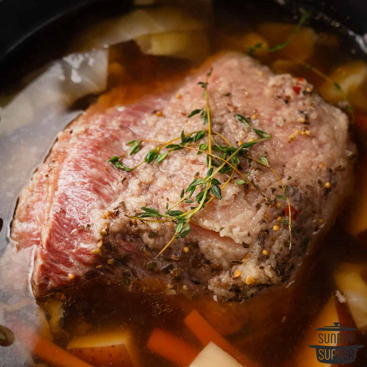 cooked corned beef in a pot of broth with vegetables
