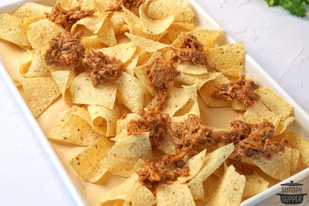 layering tortilla chips and pulled pork on a baking tray