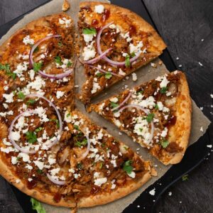 close up of pulled pork pizza on a cutting board with two slices cut out