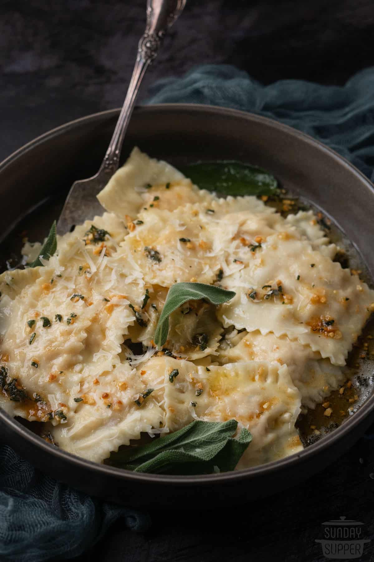 sage brown butter sauce drizzled over ravioli in a black dish