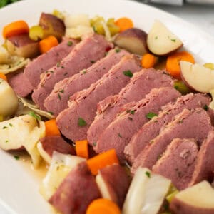 cooked sliced corned beef on a plate with veggies and broth