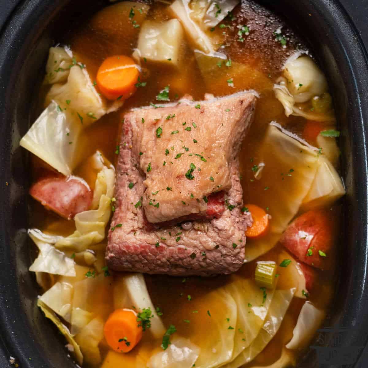 cooked corned beef in a slow cooker pot with vegetables