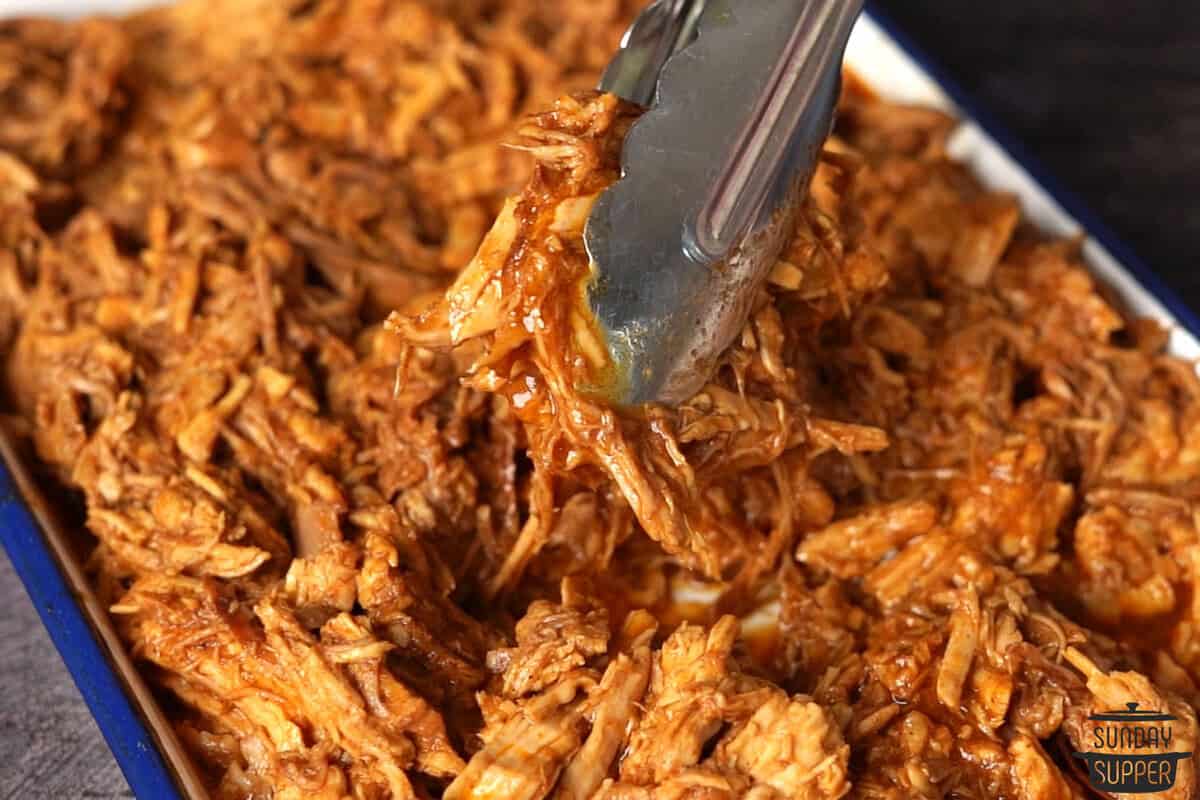 tongs filled with pulled pork over a pan