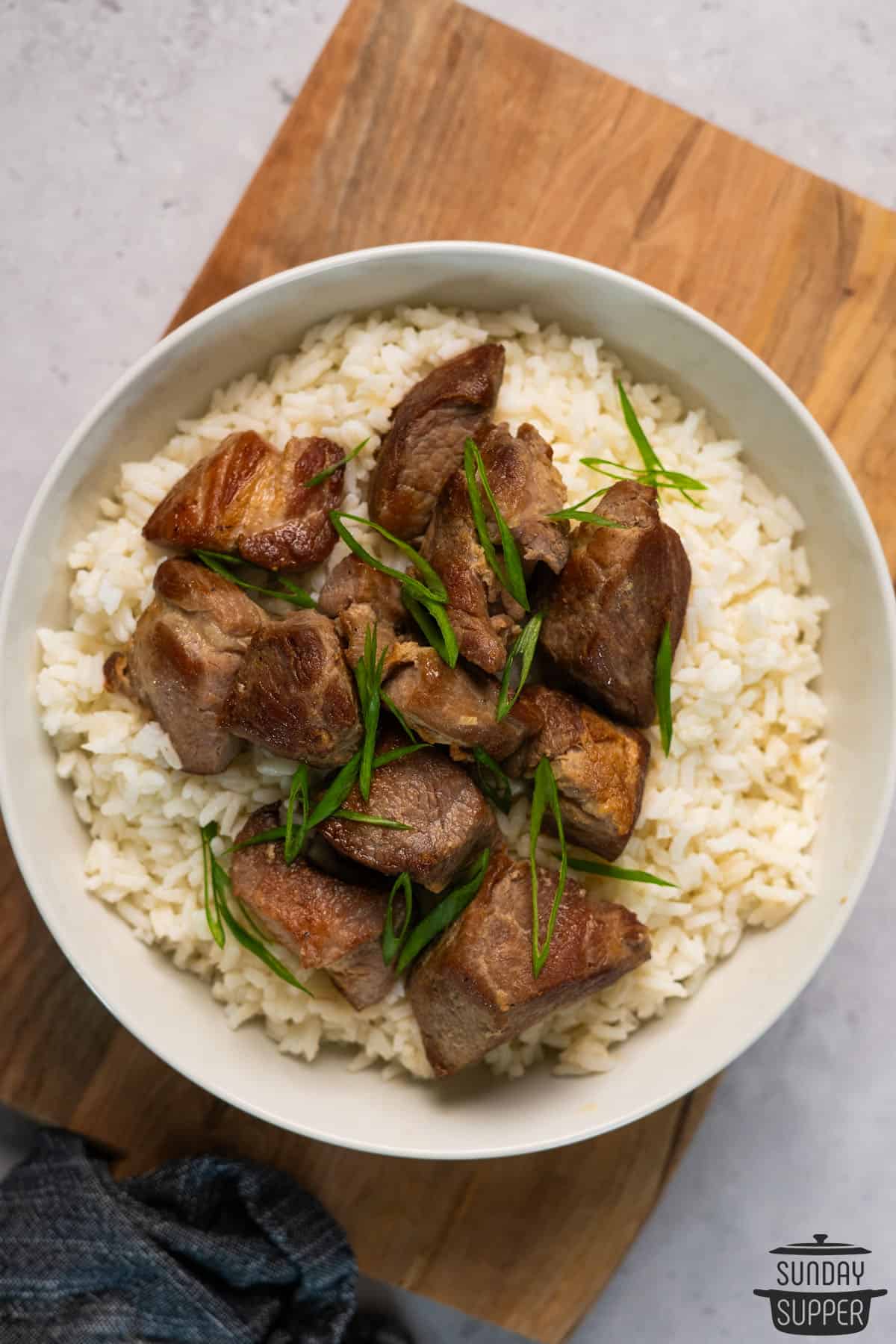 green onion and pork topped white rice in a bowl