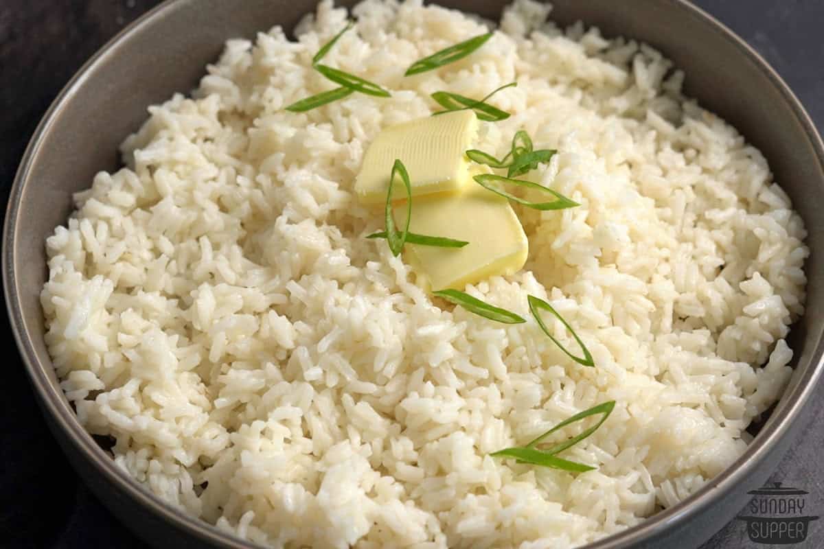 a serving bowl of white rice with extra butter and sliced green onions