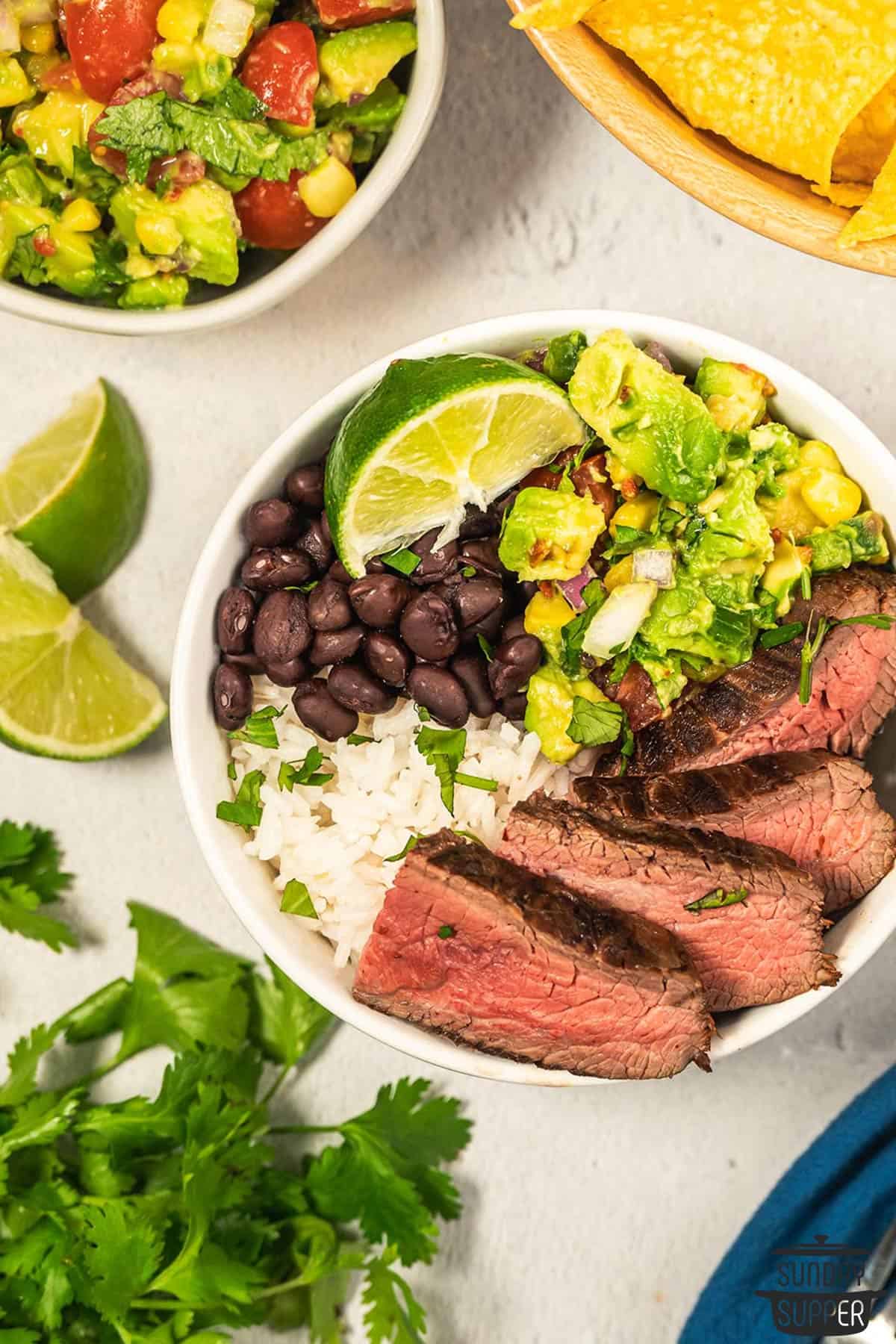 slices of flank steak in a rice bowl with avocado salsa and lime