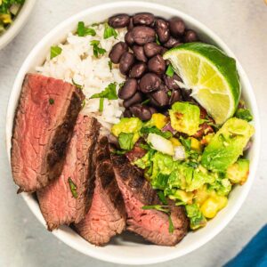 a rice bowl with black beans, lime, avocado salsa, and marinated flank steak