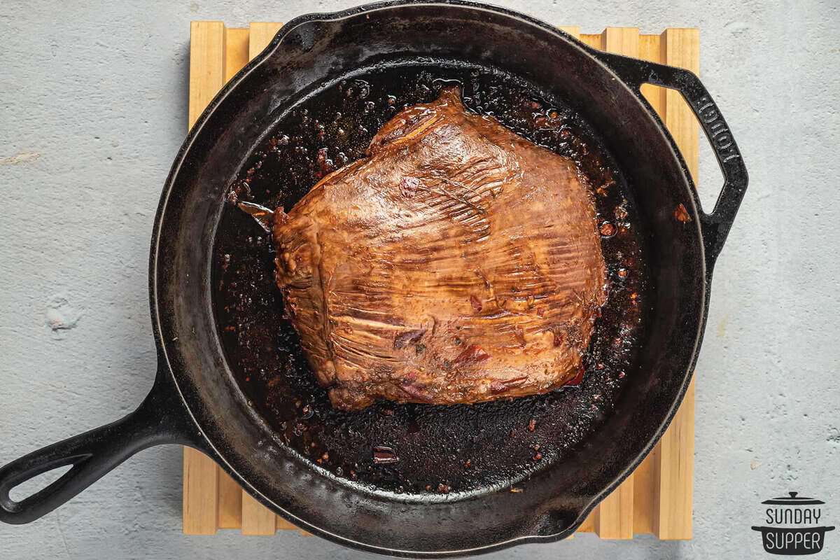 the steak being seared in a cast iron pan