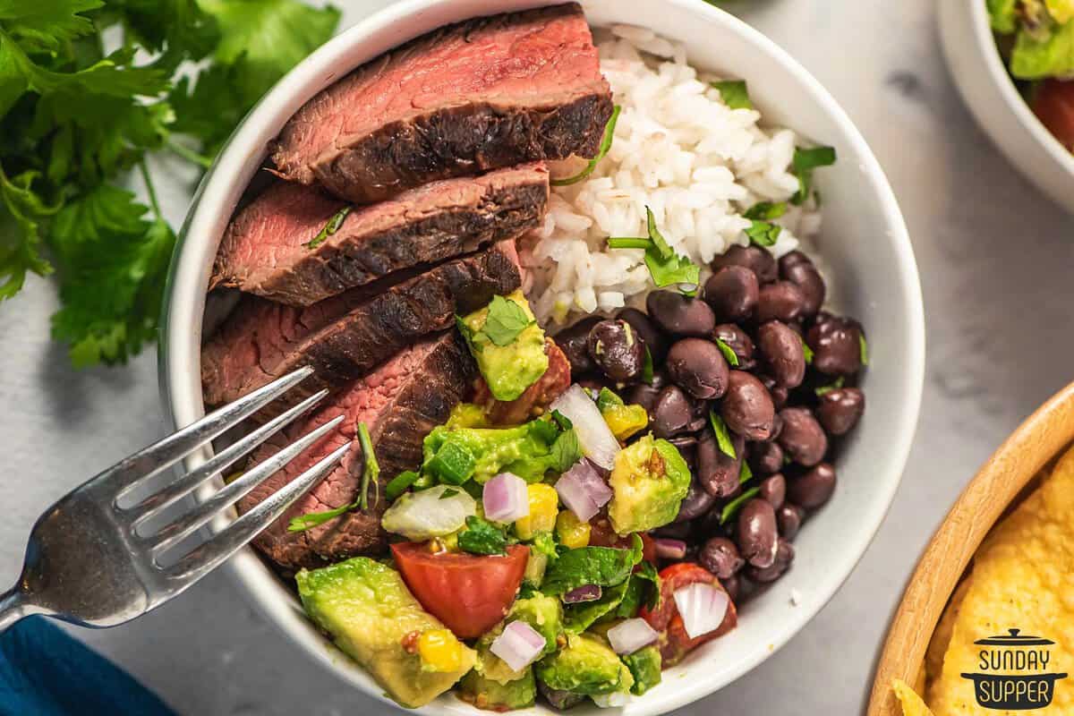 steak slices served in a rice bowl with black beans and avocado salsa