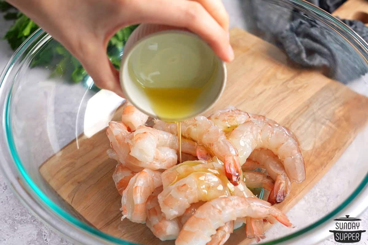 oil and lemon juice being poured on the shrimp