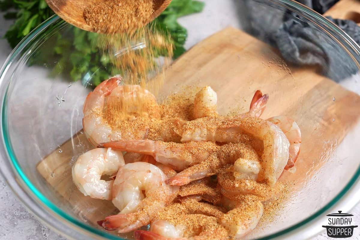 shrimp in a bowl with seasonings being poured on them