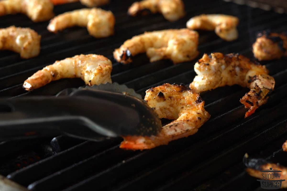 shrimp being placed on a grill with tongs
