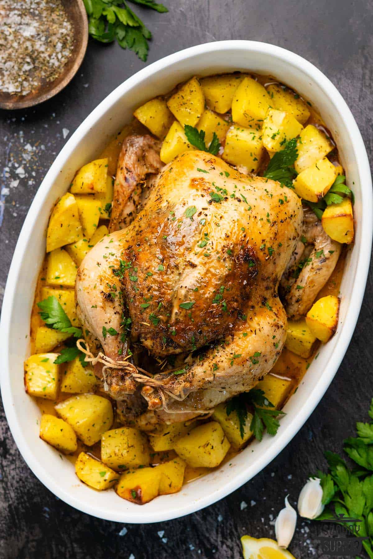 a whole roast chicken in a pan with potatoes