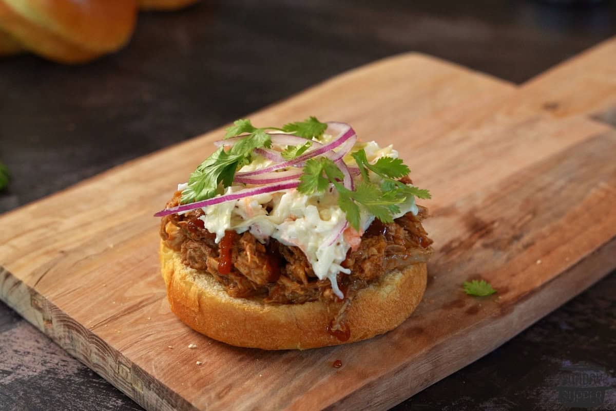 adding red onions and cilantro to pulled pork sandwich