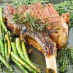 sliced tomahawk steak on a baking sheet with asparagus