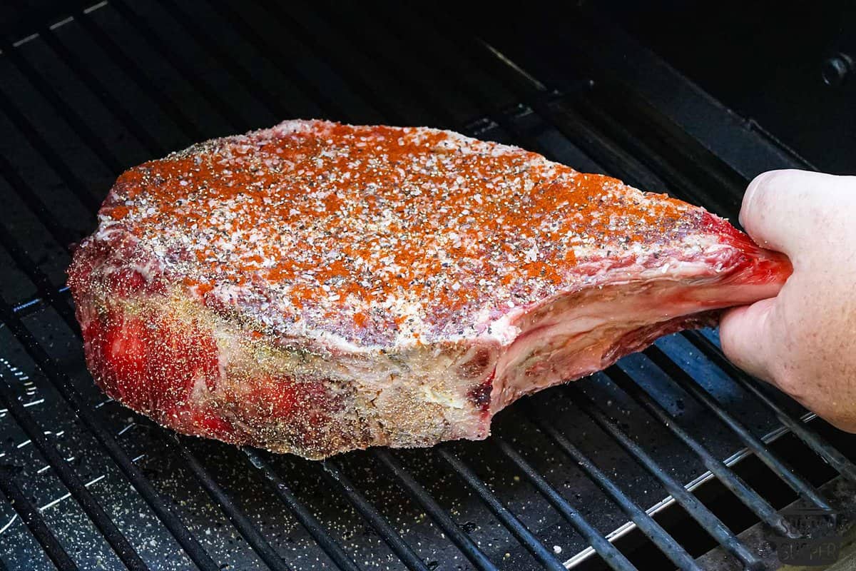 the seasoned steak being placed on the smoker