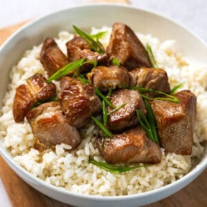 pork adobo garnished with green onions on a bowl of rice