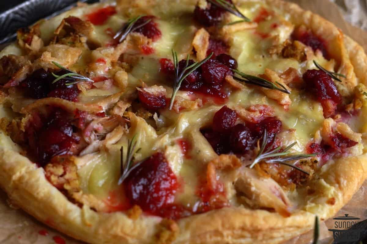 a closeup of a fully baked thanksgiving leftovers pizza with a garnish of rosemary