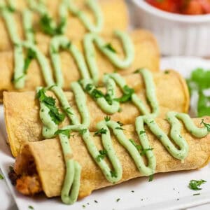 a serving dish of taquitos with lime crema and cilantro
