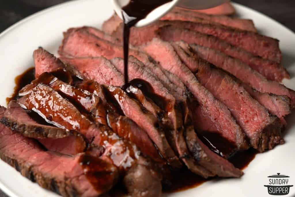 pouring marinade over london broil sliced on a plate