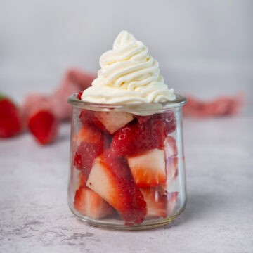 whipped cream on top of sliced strawberries in a bowl