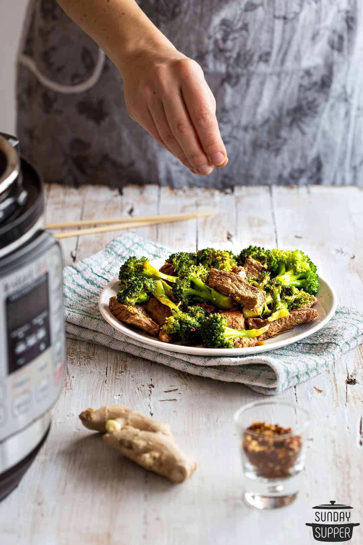 red pepper flakes being sprinkled on beef and broccoli