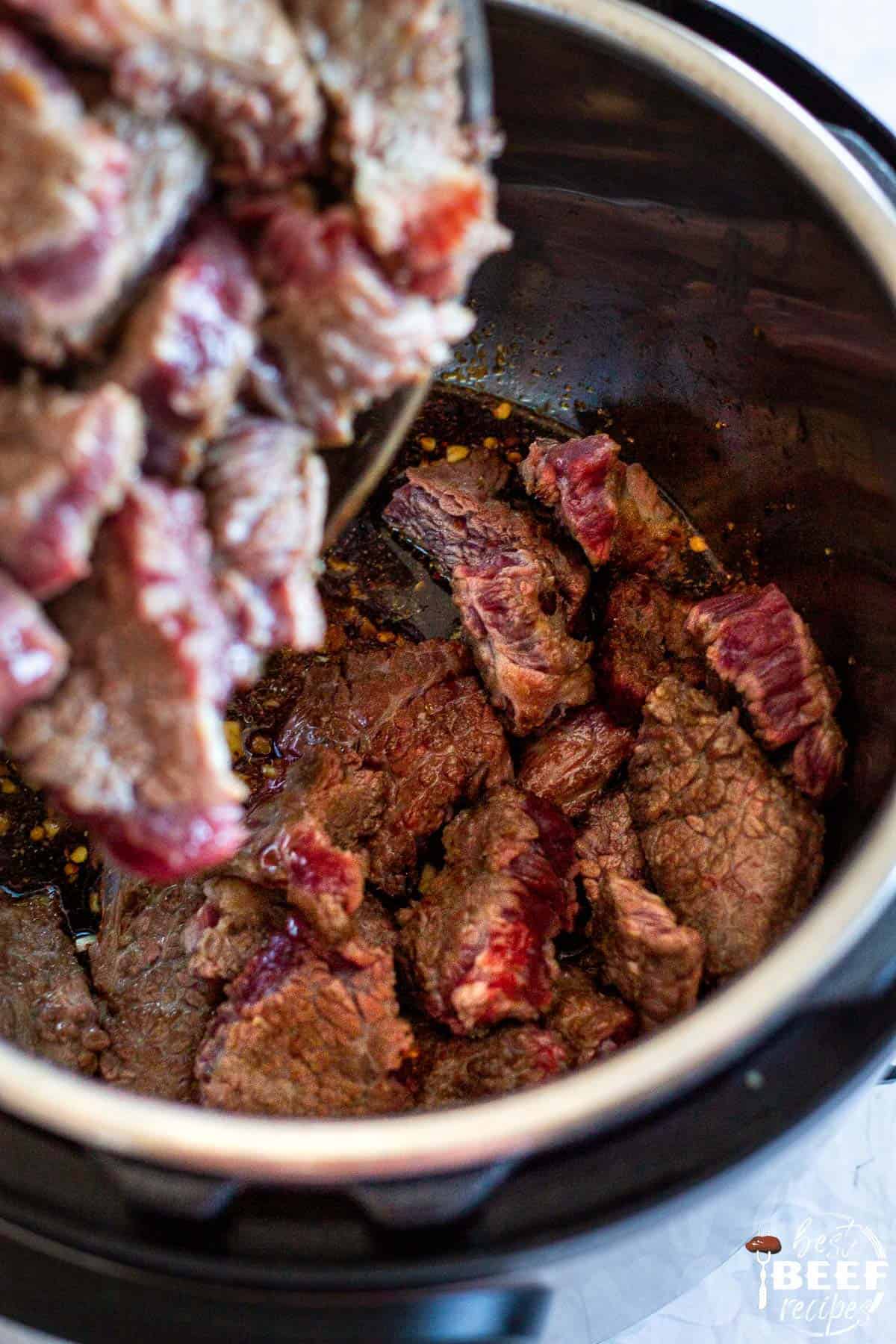 the beef being added to the sauce to pressure cook