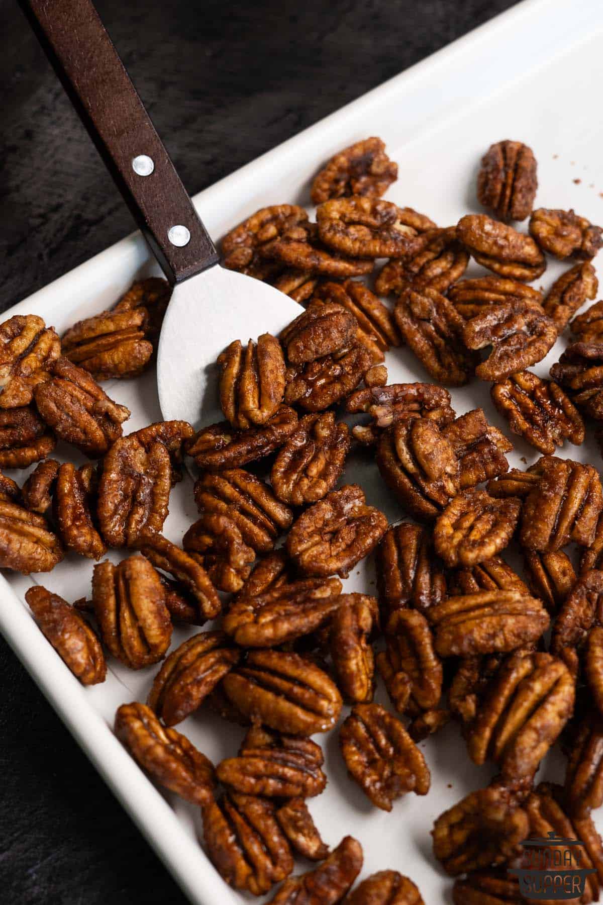 scooping candied pecans off a sheet with a spatula