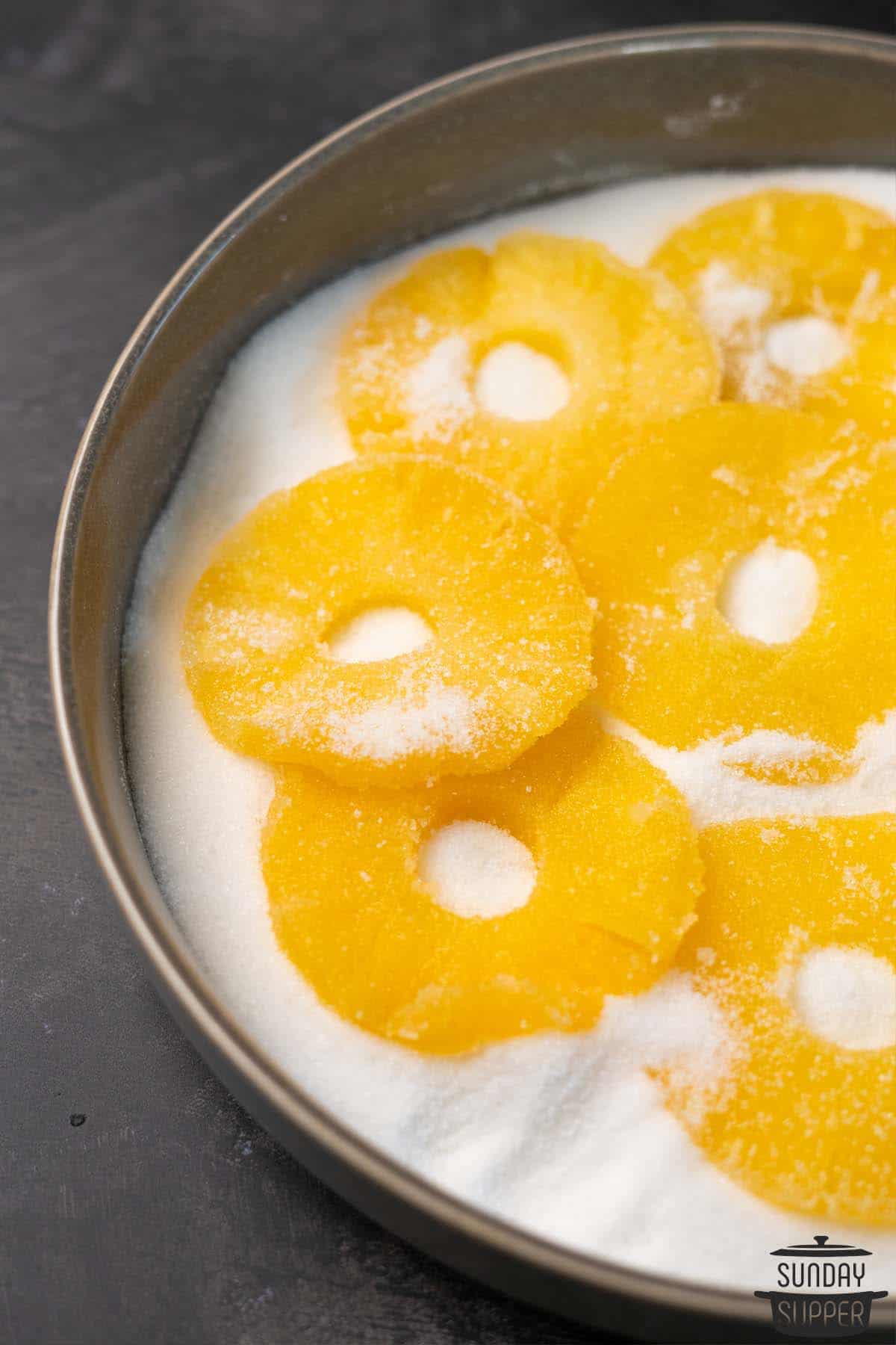 candied pineapple rings in a dish of sugar