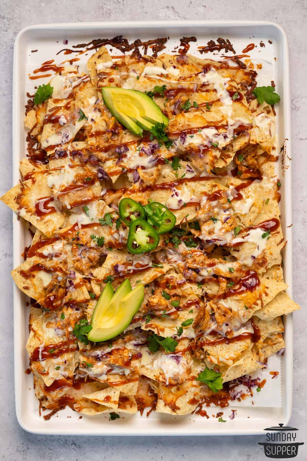 a top down view of a baking dish of baked chicken nachos with toppings